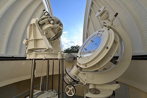 Telescopi e strumenti astronomici all'interno di un osservatorio, sotto una caratteristica cupola bianca.